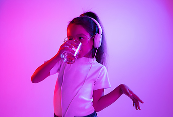 Image showing Portrait of little girl in headphones on purple gradient background in neon light