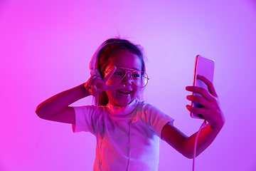 Image showing Portrait of little girl in headphones on purple gradient background in neon light