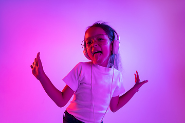 Image showing Portrait of little girl in headphones on purple gradient background in neon light