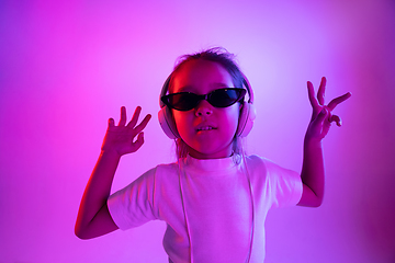 Image showing Portrait of little girl in headphones on purple gradient background in neon light