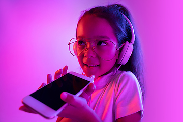 Image showing Portrait of little girl in headphones on purple gradient background in neon light