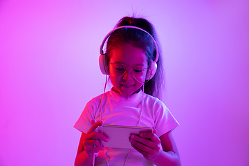 Image showing Portrait of little girl in headphones on purple gradient background in neon light