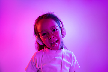 Image showing Portrait of little girl in headphones on purple gradient background in neon light