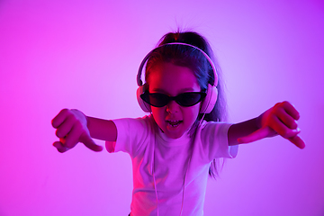 Image showing Portrait of little girl in headphones on purple gradient background in neon light