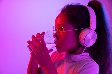 Image showing Portrait of little girl in headphones on purple gradient background in neon light