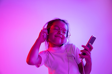 Image showing Portrait of little girl in headphones on purple gradient background in neon light