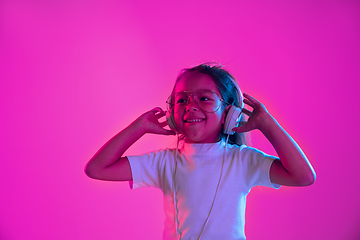 Image showing Portrait of little girl in headphones on purple gradient background in neon light