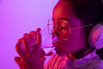 Image showing Portrait of little girl in headphones on purple gradient background in neon light