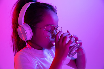 Image showing Portrait of little girl in headphones on purple gradient background in neon light