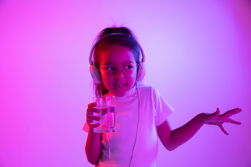 Image showing Portrait of little girl in headphones on purple gradient background in neon light