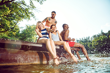 Image showing Group of happy friends having fun while sitting and laughting on the pier on river