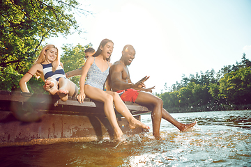 Image showing Group of happy friends having fun while sitting and laughting on the pier on river