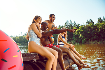 Image showing Group of happy friends having fun while sitting and laughting on the pier on river