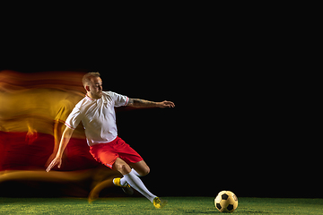 Image showing Male soccer player kicking ball on dark background in mixed light