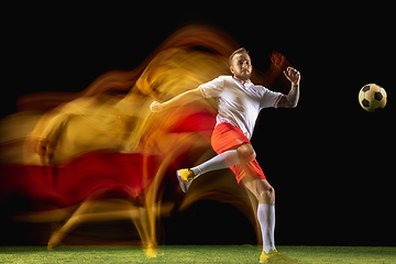 Image showing Male soccer player kicking ball on dark background in mixed light