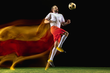 Image showing Male soccer player kicking ball on dark background in mixed light