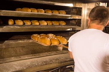 Image showing bakery worker taking out freshly baked breads