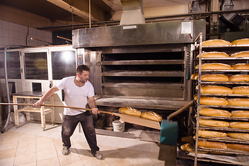 Image showing bakery worker taking out freshly baked breads