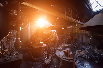 Image showing blacksmith manually forging the molten metal with sunlight throu