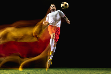 Image showing Male soccer player kicking ball on dark background in mixed light