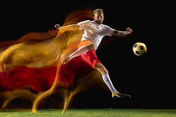 Image showing Male soccer player kicking ball on dark background in mixed light