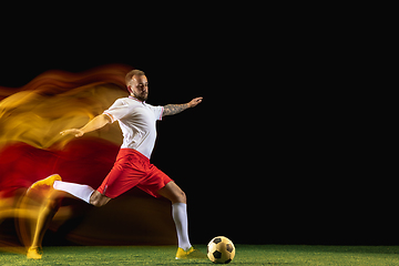 Image showing Male soccer player kicking ball on dark background in mixed light