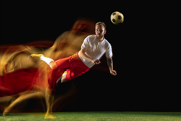 Image showing Male soccer player kicking ball on dark background in mixed light