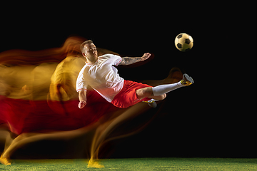 Image showing Male soccer player kicking ball on dark background in mixed light