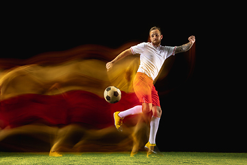 Image showing Male soccer player kicking ball on dark background in mixed light