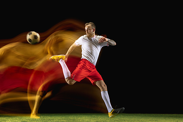 Image showing Male soccer player kicking ball on dark background in mixed light