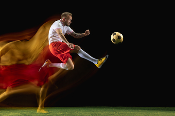 Image showing Male soccer player kicking ball on dark background in mixed light