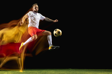 Image showing Male soccer player kicking ball on dark background in mixed light