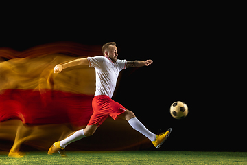 Image showing Male soccer player kicking ball on dark background in mixed light