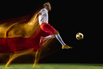 Image showing Male soccer player kicking ball on dark background in mixed light