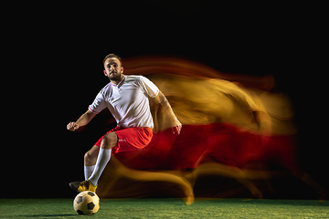 Image showing Male soccer player kicking ball on dark background in mixed light