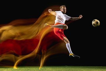 Image showing Male soccer player kicking ball on dark background in mixed light