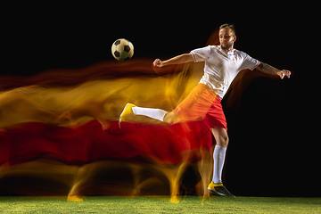 Image showing Male soccer player kicking ball on dark background in mixed light