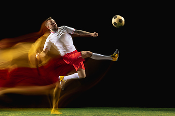 Image showing Male soccer player kicking ball on dark background in mixed light