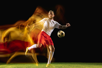 Image showing Male soccer player kicking ball on dark background in mixed light