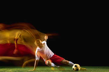 Image showing Male soccer player kicking ball on dark background in mixed light