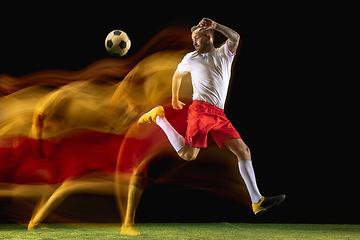 Image showing Male soccer player kicking ball on dark background in mixed light