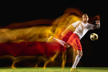 Image showing Male soccer player kicking ball on dark background in mixed light