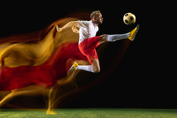 Image showing Male soccer player kicking ball on dark background in mixed light