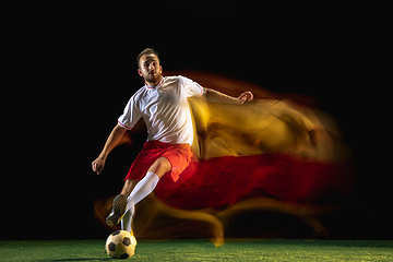 Image showing Male soccer player kicking ball on dark background in mixed light