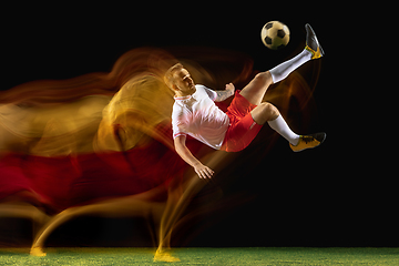 Image showing Male soccer player kicking ball on dark background in mixed light