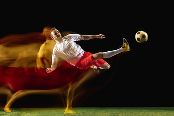 Image showing Male soccer player kicking ball on dark background in mixed light