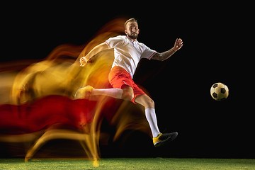 Image showing Male soccer player kicking ball on dark background in mixed light