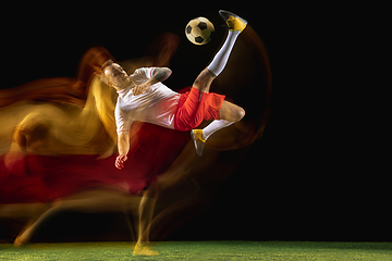 Image showing Male soccer player kicking ball on dark background in mixed light