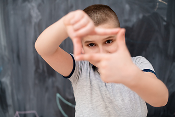 Image showing happy boy making hand frame gesture in front of chalkboard
