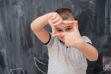 Image showing happy boy making hand frame gesture in front of chalkboard